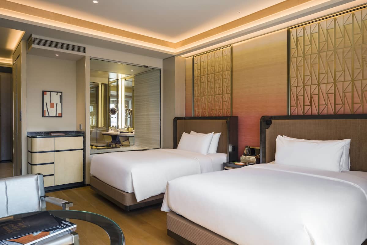 A hotel room with two beds, a desk, and a mirror.