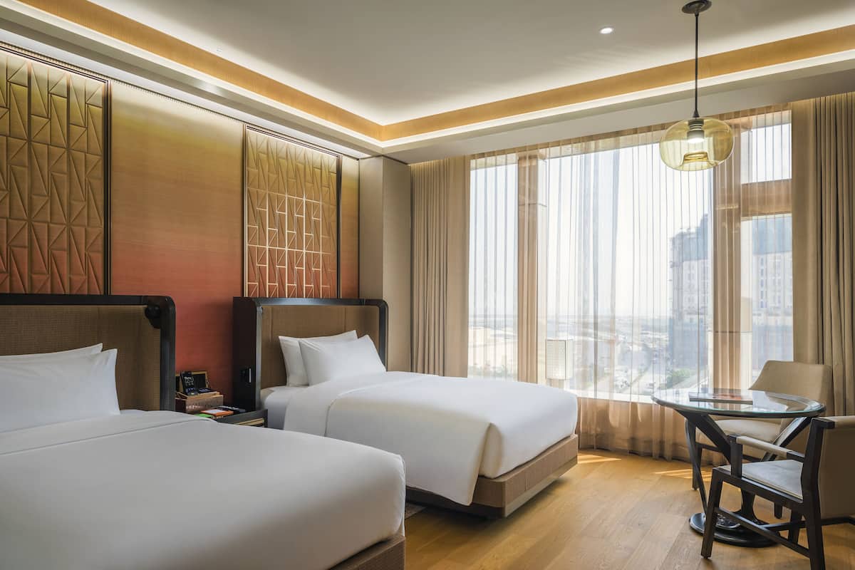 A hotel room with two beds, a small table, and a view of the city.