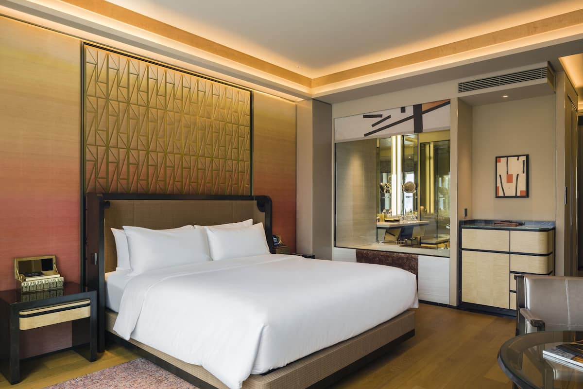 A modern hotel room with a large bed, a bedside table, a mirror, and a small seating area.