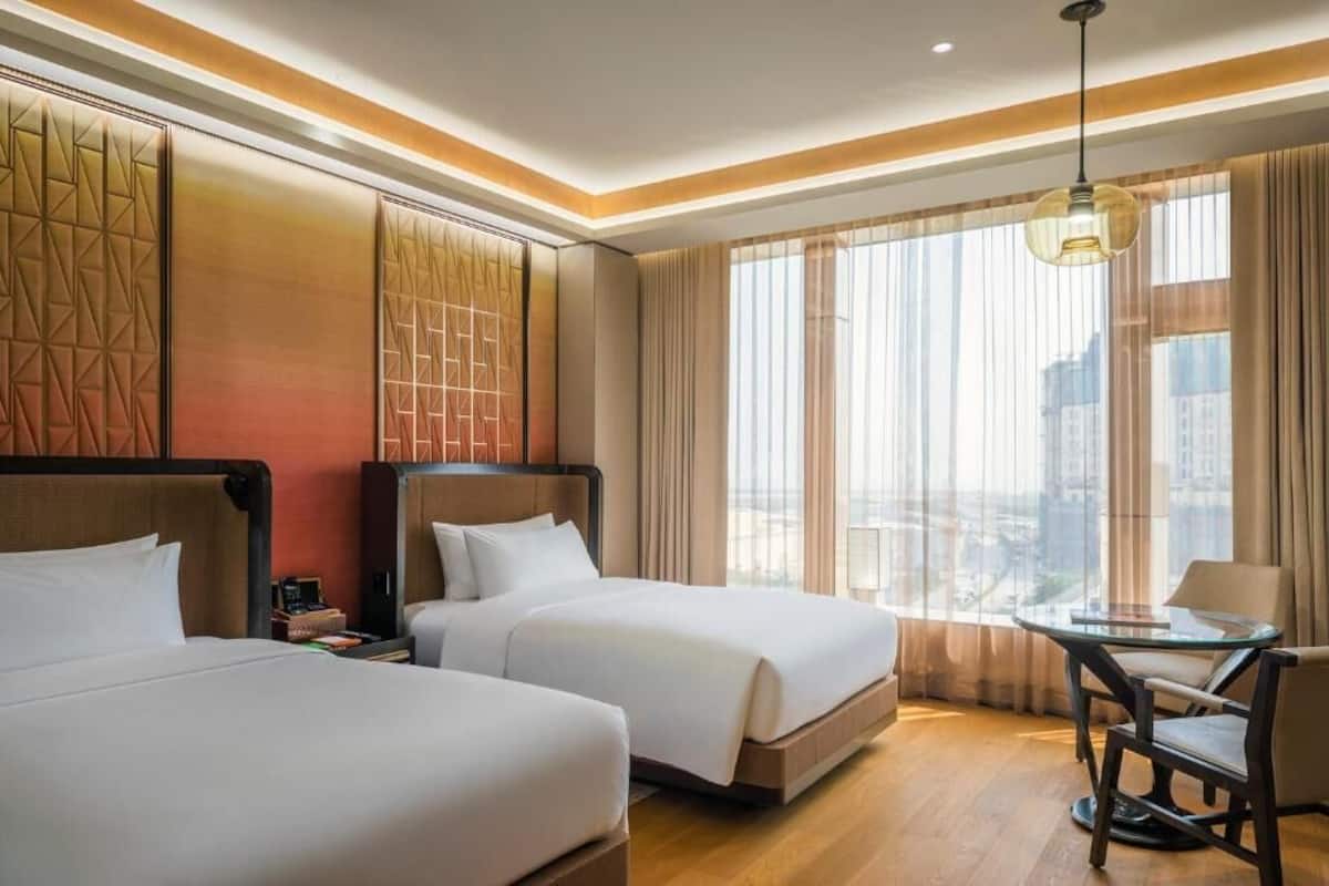 A hotel room with two beds, a small table, and a view of the city.