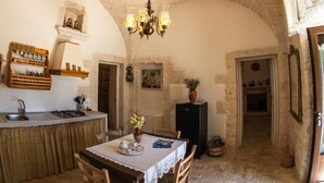 A stone-walled kitchen with a dining table and chairs, a chandelier, and a small island with a sink and storage. - Agriturismo Grotta di Figazzano (Ostuni)