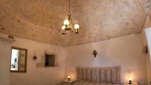 A bedroom with a vaulted ceiling, a bed with a striped bedspread, bedside lamps, and a small nightstand. - Agriturismo Grotta di Figazzano (Ostuni)