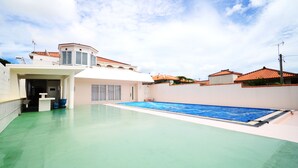 An indoor swimming pool with a green floor, surrounded by white walls and a white building with a red roof. - Hotel Kaiho Shishinomori (Ishigaki)