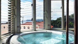 A hot tub with a view of buildings and mountains through large windows. - Hotel Kaiho Shishinomori (Ishigaki)
