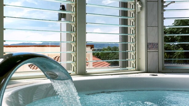 A hot tub with water flowing, a view of the sky, and a glimpse of buildings and trees in the background. - Hotel Kaiho Shishinomori (Ishigaki)