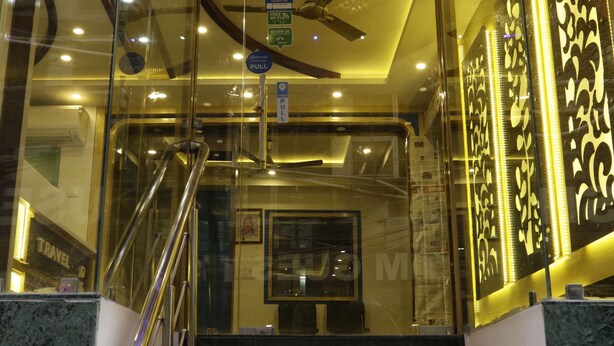 A staircase leading to a lobby with a ceiling fan, glass railings, and decorative wall panels. - Hotel Pink City (New Delhi)