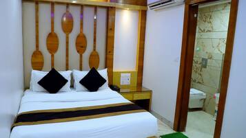 A hotel room with a bed, wooden headboard, a bedside table with a phone, and a bathroom visible through an open door.