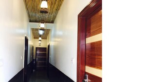 A hallway with a wooden door on the right, a black and white wall, and a ceiling with hanging lights. - Hotel Pink City (New Delhi)