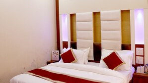 A neatly made bed with white and red bedding, a ceiling fan, and recessed lighting. - Hotel Pink City (New Delhi)