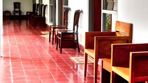 A corridor with red tiled flooring, wooden benches, and large windows.
