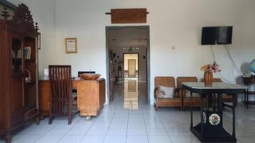 A spacious living area with a wooden cabinet, a television mounted on the wall, and a dining table with chairs.