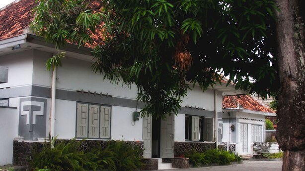 A two-story house with a tiled roof, a cross on the wall, and a front door.
