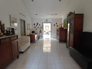 A spacious room with a tiled floor, a sofa, a cabinet, and a door leading to another area. - Ndalem Mantrigawen (Yogyakarta)
