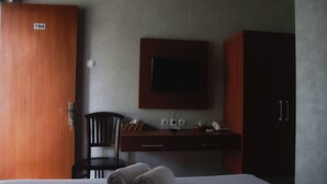 A hotel room with a bed, a desk with a flat-screen TV, a chair, and a wardrobe.