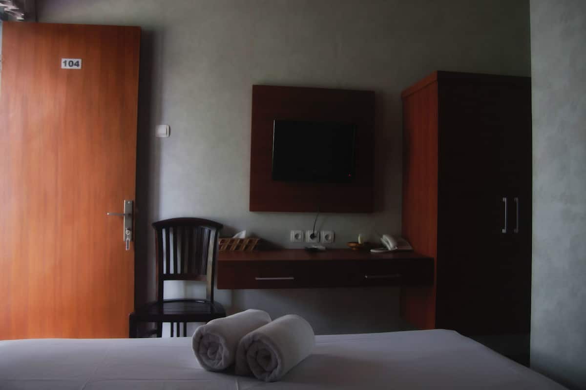 A hotel room with a bed, a desk with a flat-screen TV, a chair, and a wardrobe.
