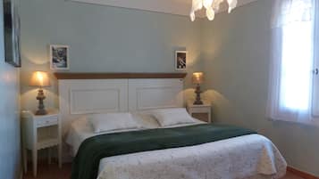 A bedroom with a bed, two bedside tables, a hanging light fixture, and a window with curtains.