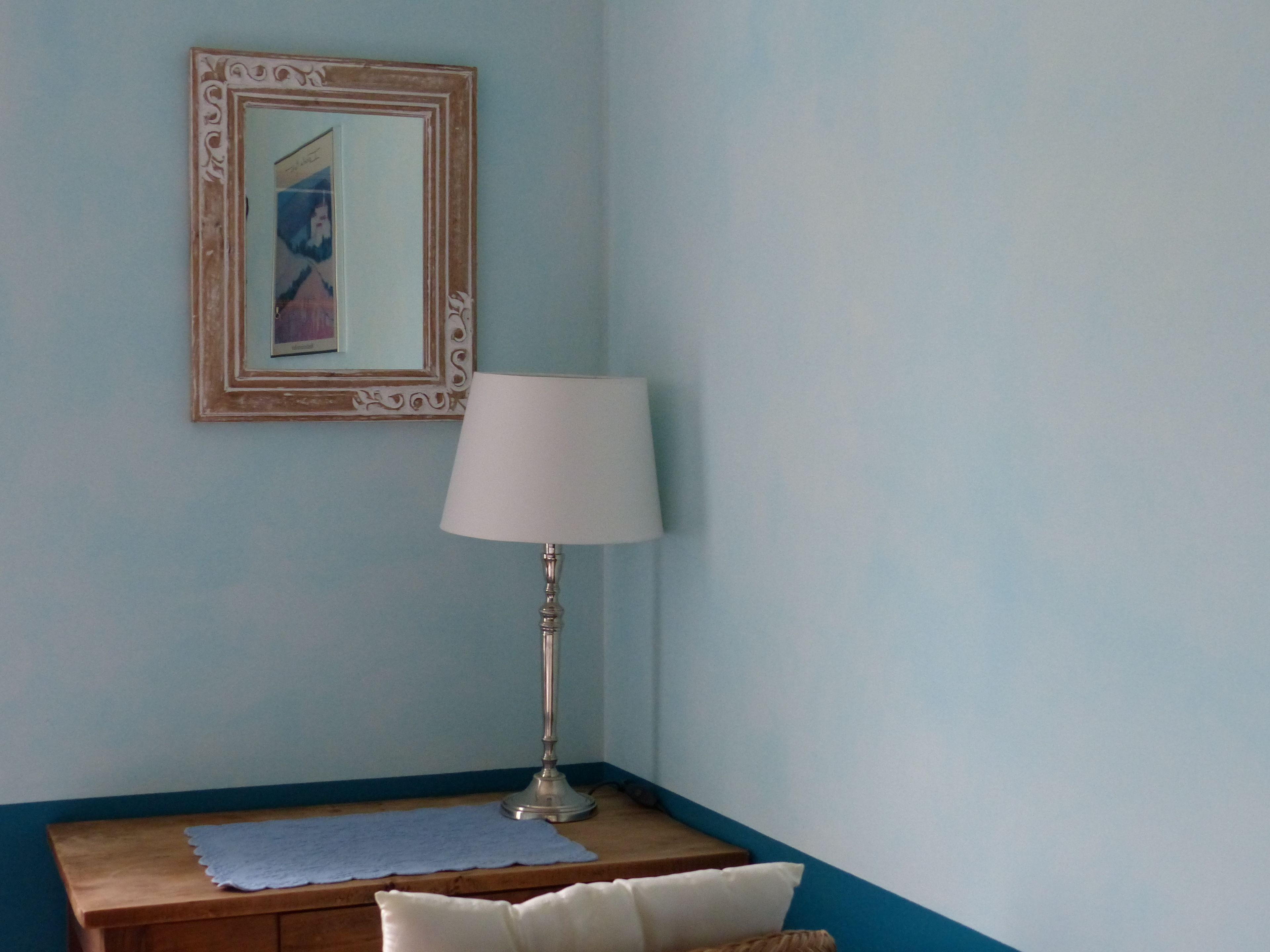 Een kamer met een houten nachtkastje, een witte lamp en een lijst met een afbeelding aan de muur.