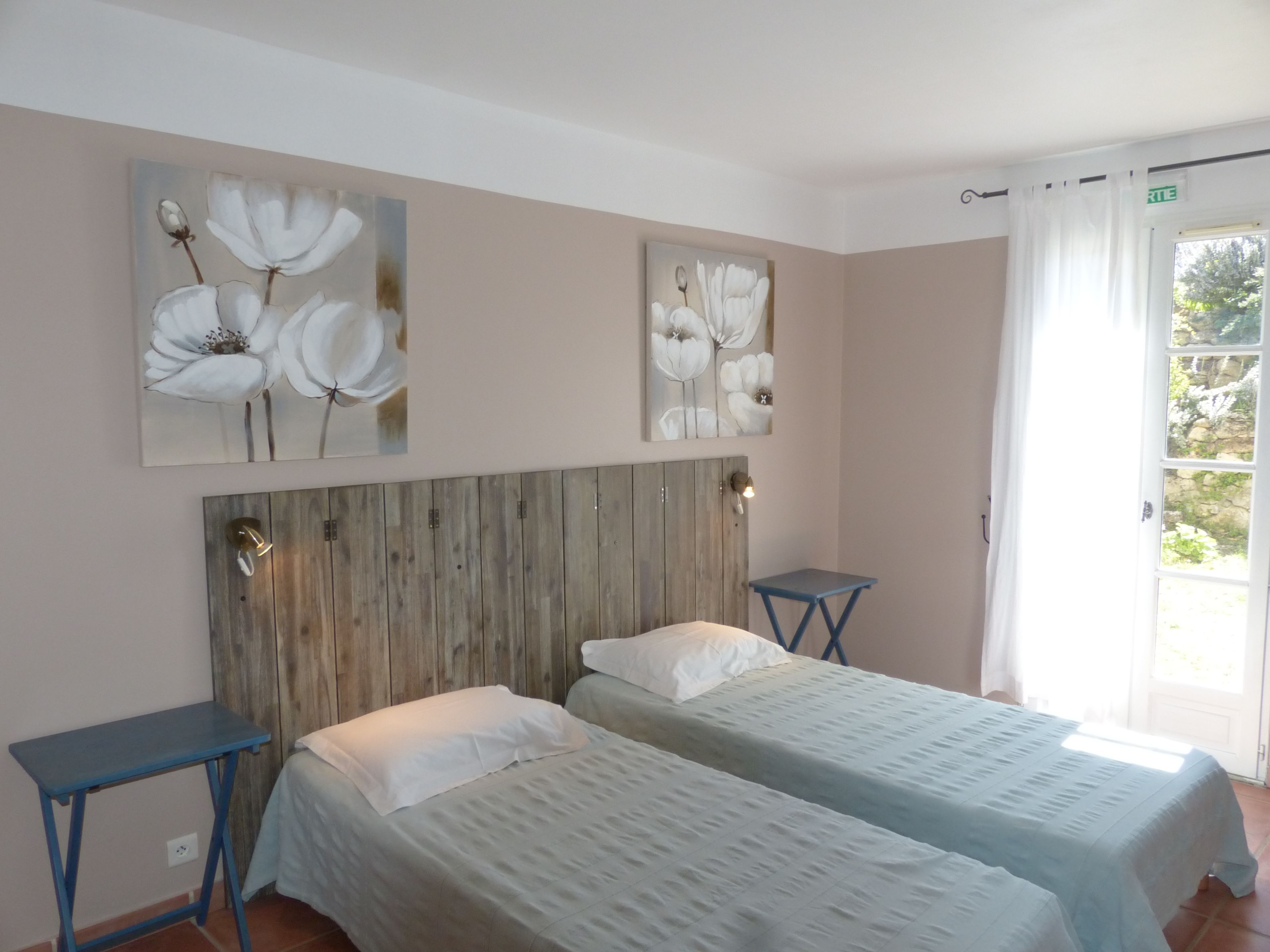 Una habitación con dos camas, cabecero de madera, decoración en la pared y una ventana con cortinas.