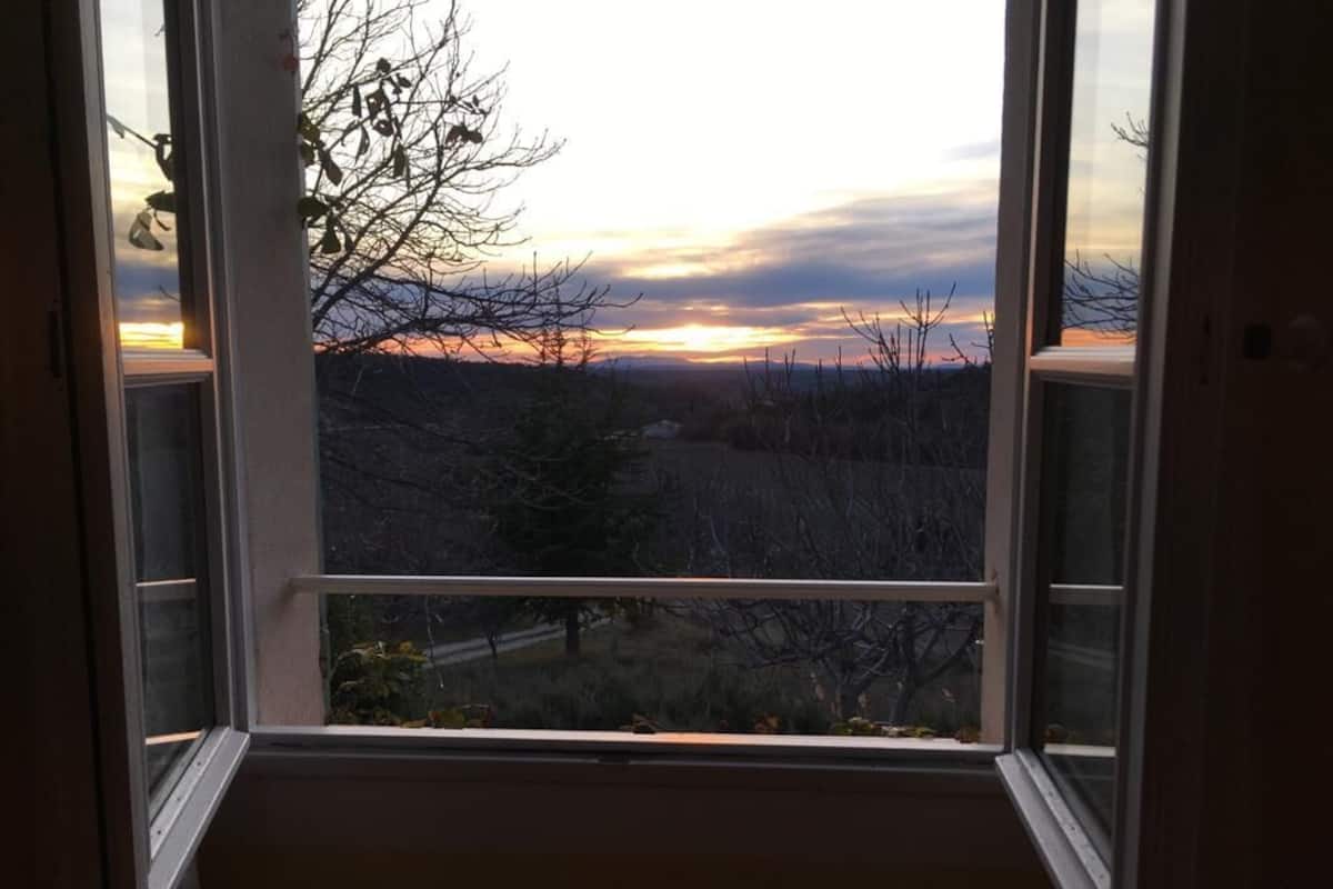 Une fenêtre donnant sur un paysage boisé, avec une vue sur le coucher du soleil.