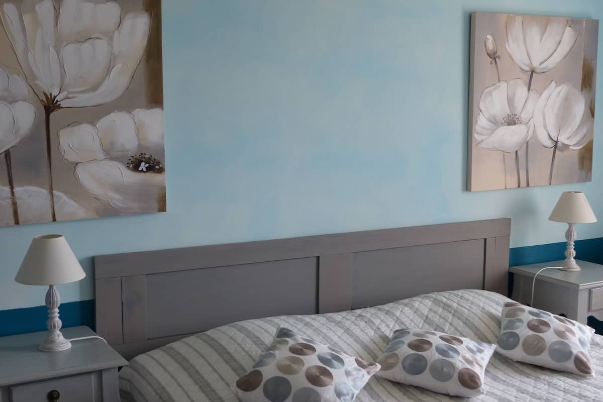 Une chambre à coucher avec un lit, deux tables de chevet, une lampe sur chacune, et un mur orné de tableaux représentant des motifs floraux.