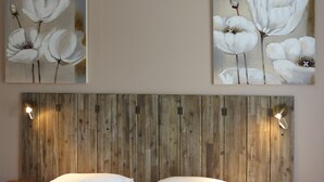 A bedroom with a wooden headboard, two wall-mounted lamps, and two paintings of white flowers. - La Ferme du Petit Ségriès (Moustiers-Sainte-Marie)