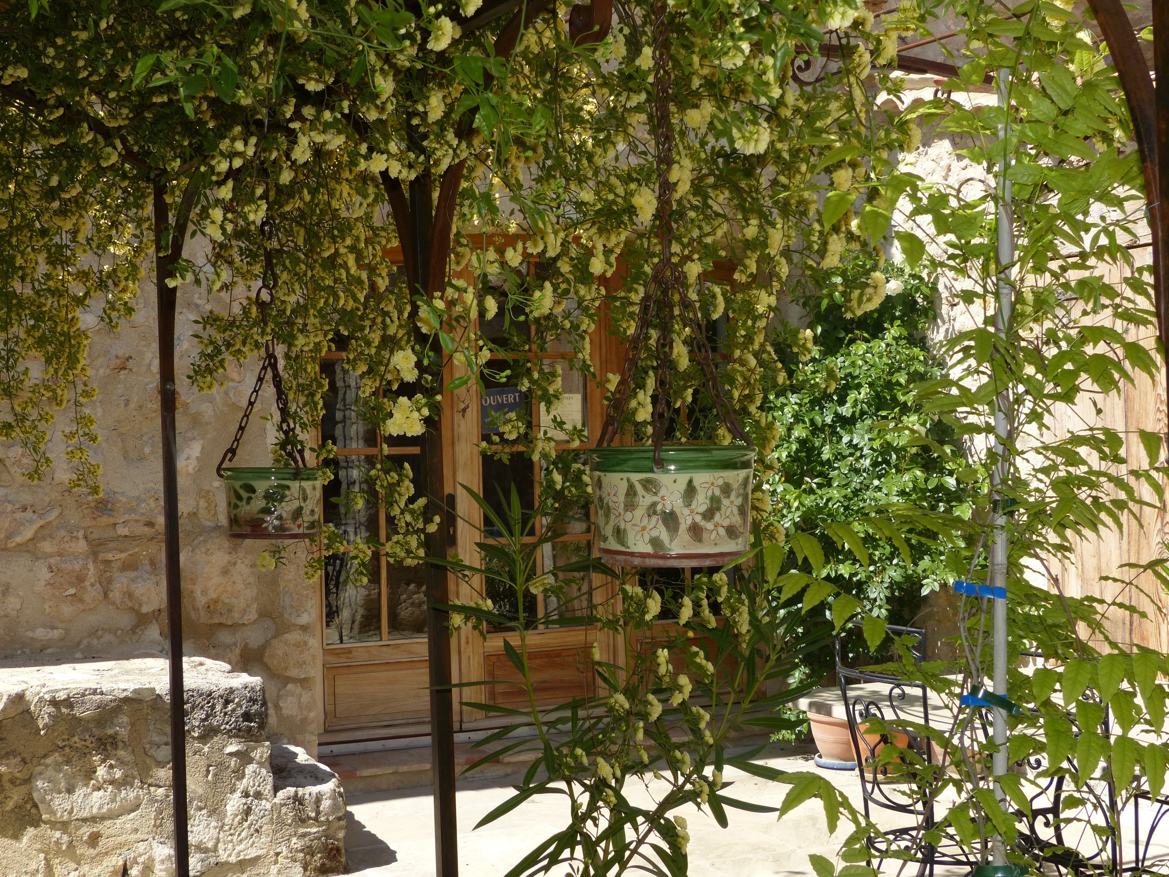A stone building with a wooden door and windows, surrounded by greenery and potted plants.