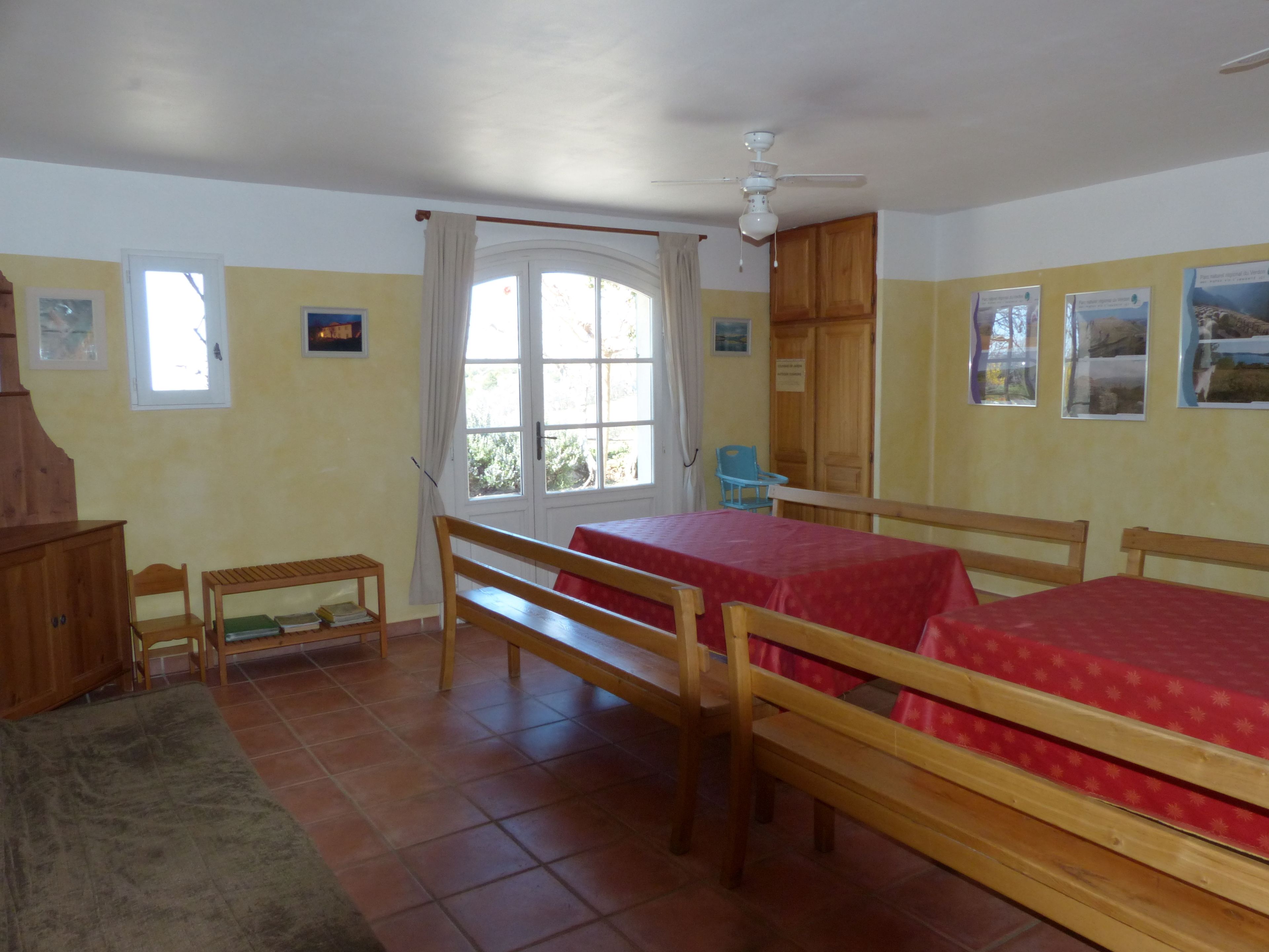 A room with two wooden beds, a wooden bench, a small table, and a ceiling fan.