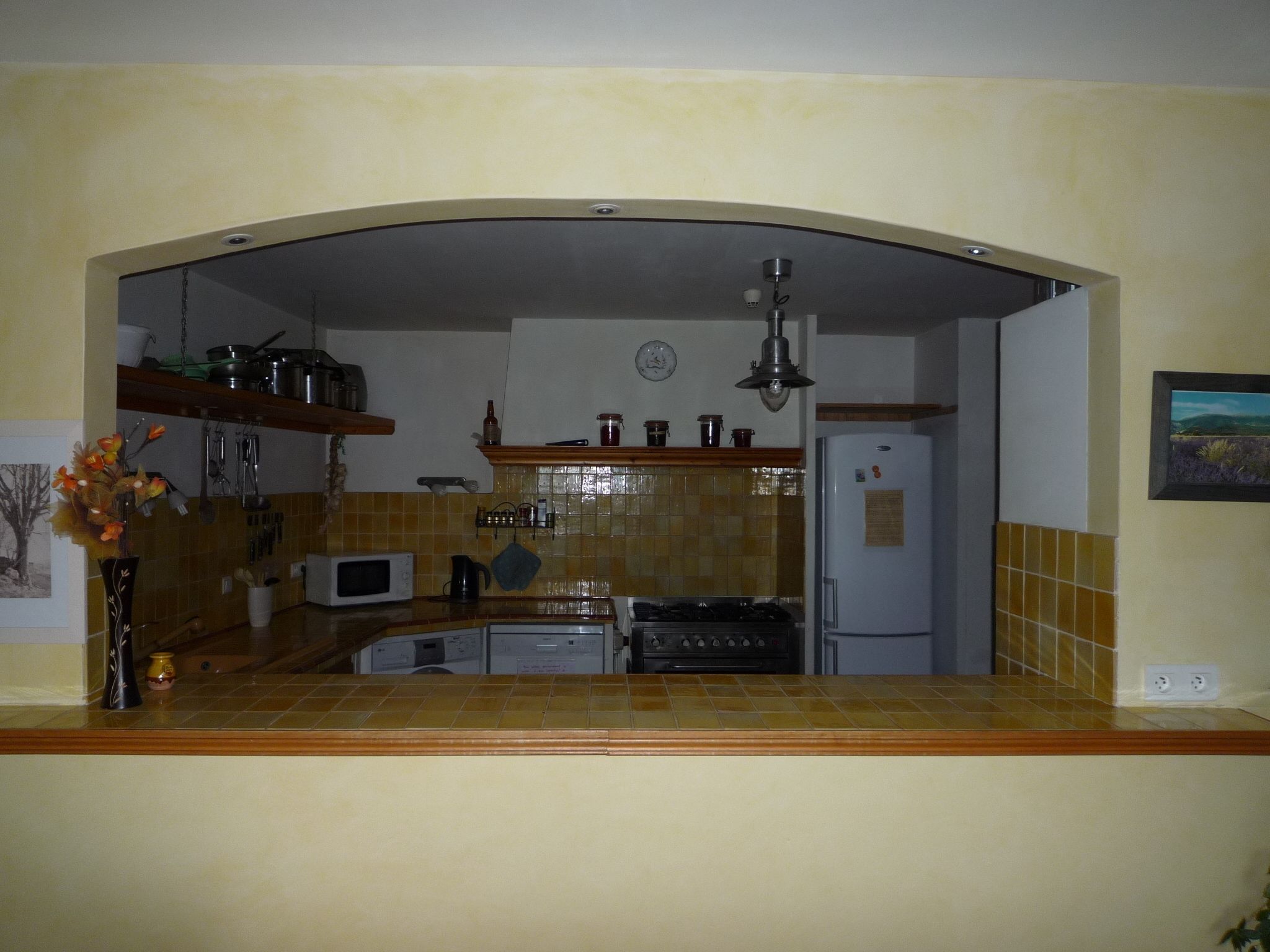 Eine Küche mit Mikrowelle, Herd und Kühlschrank. An der Wand hängt eine Uhr und eine Deckenleuchte.