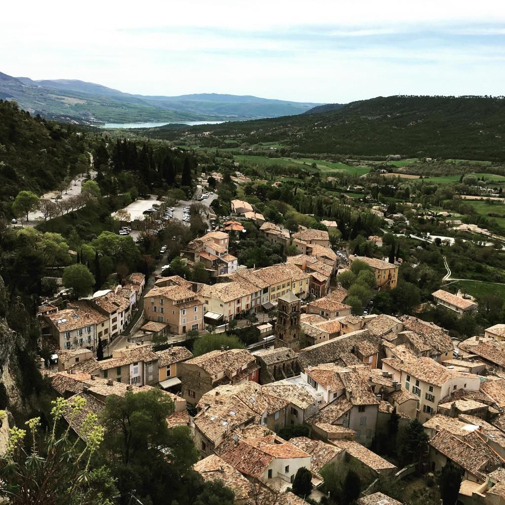 A town with terracotta-roofed buildings, a river, and surrounding hills.