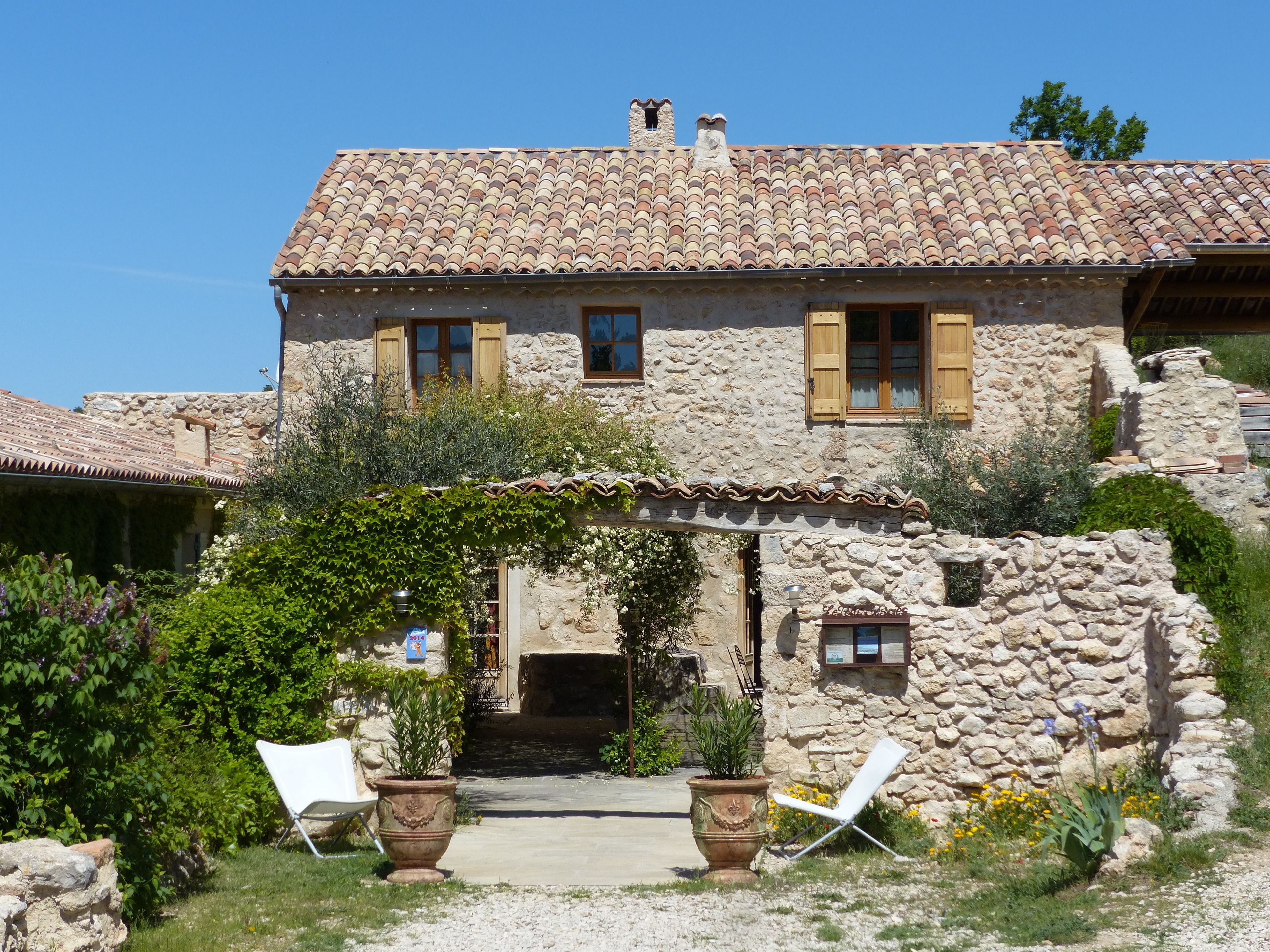 A stone house with a tiled roof, a stone facade, and a small porch with potted plants.