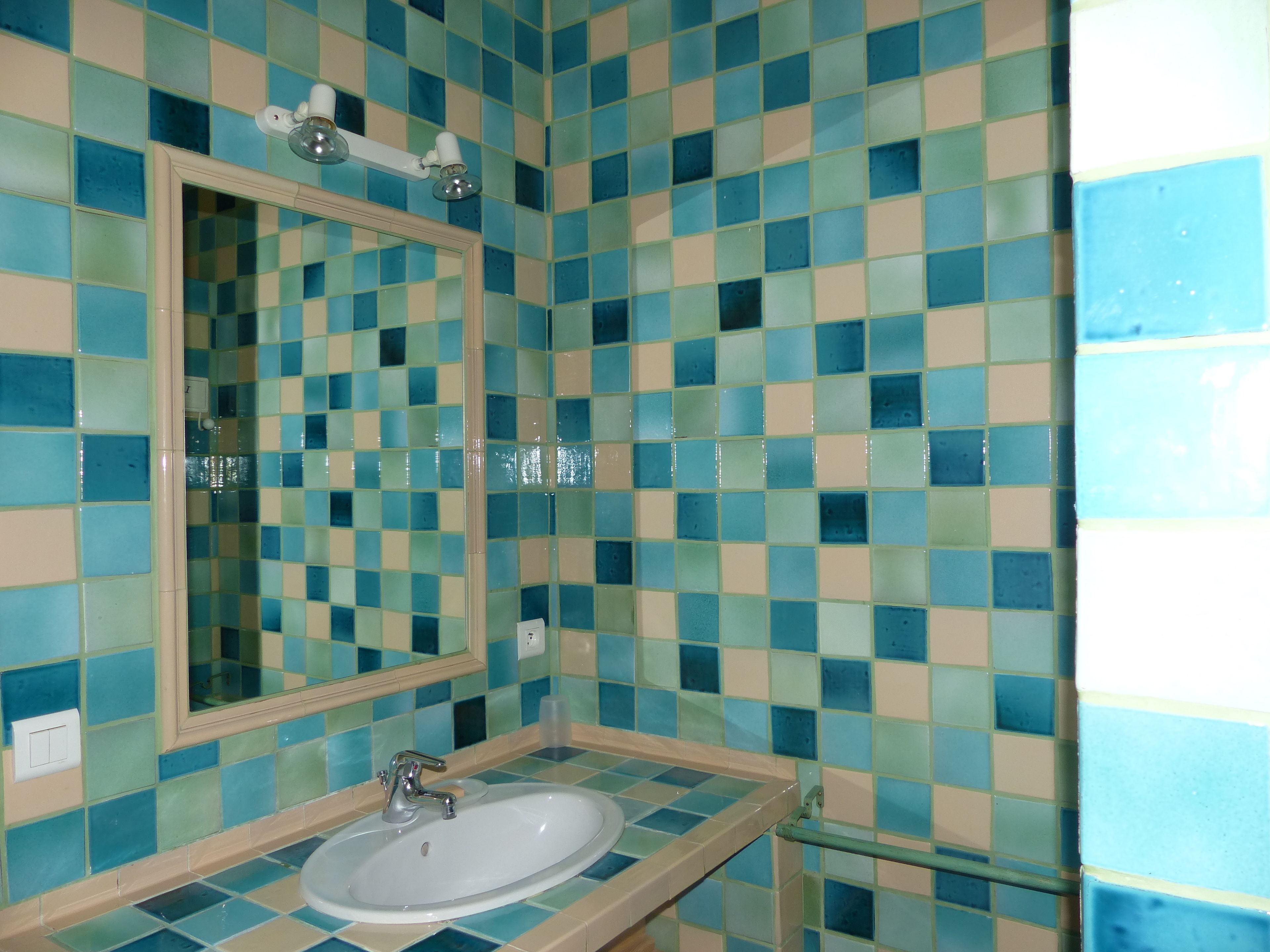 Un baño con un salpicadero de azulejos a cuadros, un espejo y un lavabo.