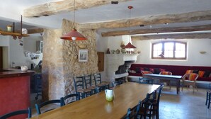 A spacious dining area with a wooden table and chairs, a stone wall, and a red hanging light fixture. - La Ferme du Petit Ségriès (Moustiers-Sainte-Marie)