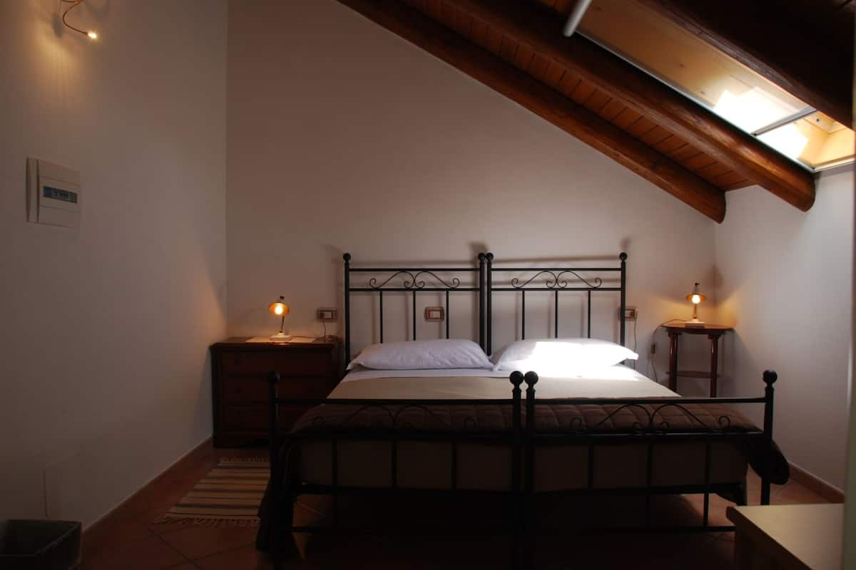 Een slaapkamer met een bed, twee nachtkastjes, een houten plafond en een dakraam.