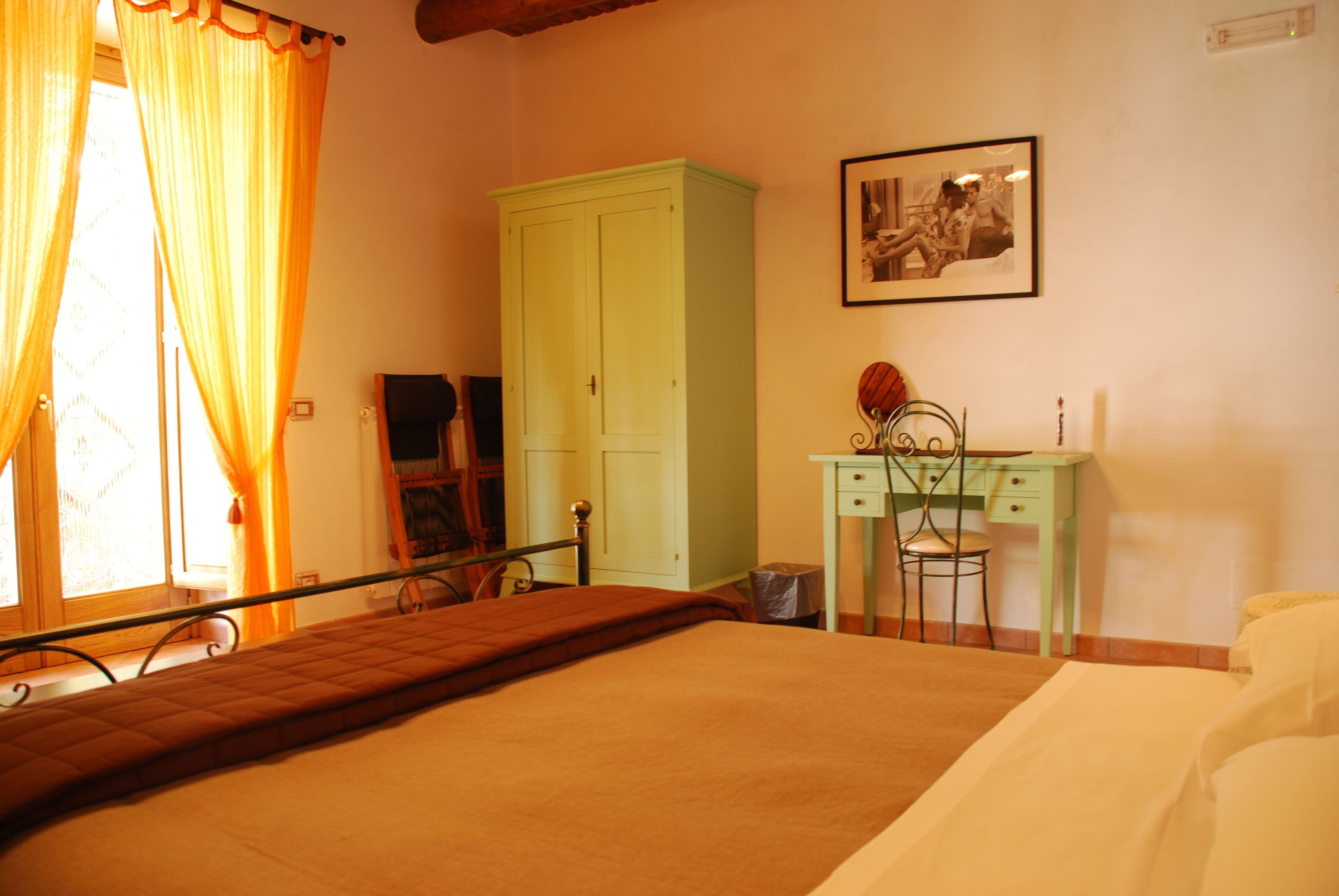 A bedroom with a bed, a desk, a chair, a wardrobe, and a framed picture on the wall.