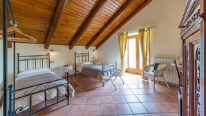 A bedroom with two beds, wooden ceiling beams, tiled floor, and a chair by the window. - Beata Solitudo B&B (Agerola)