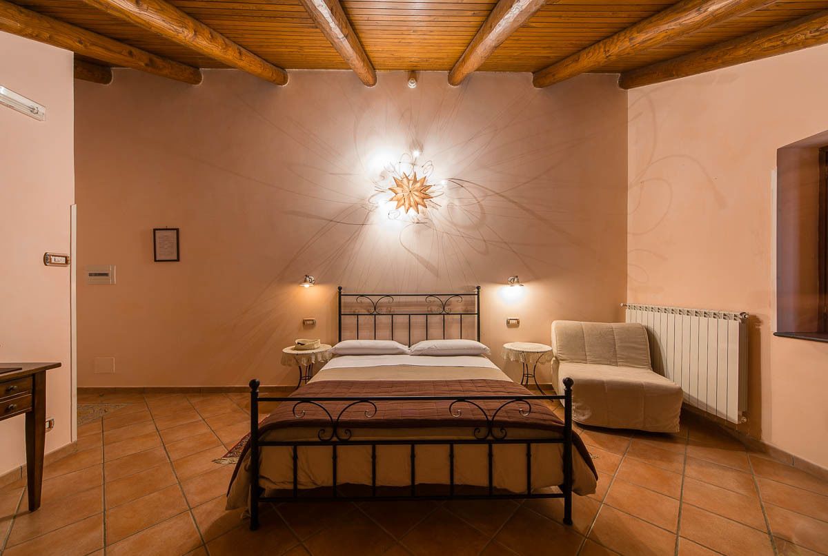Un dormitorio con cama, mesitas de noche, una silla, un radiador y un accesorio de luz en la pared.