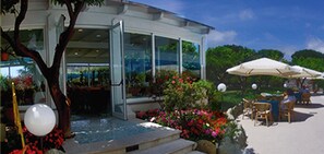 Un edificio moderno con fachada de vidrio, zona de estar exterior con sombrillas y piscina.