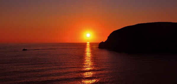 Un coucher de soleil sur une mer calme, avec la silhouette d'une falaise à l'horizon.