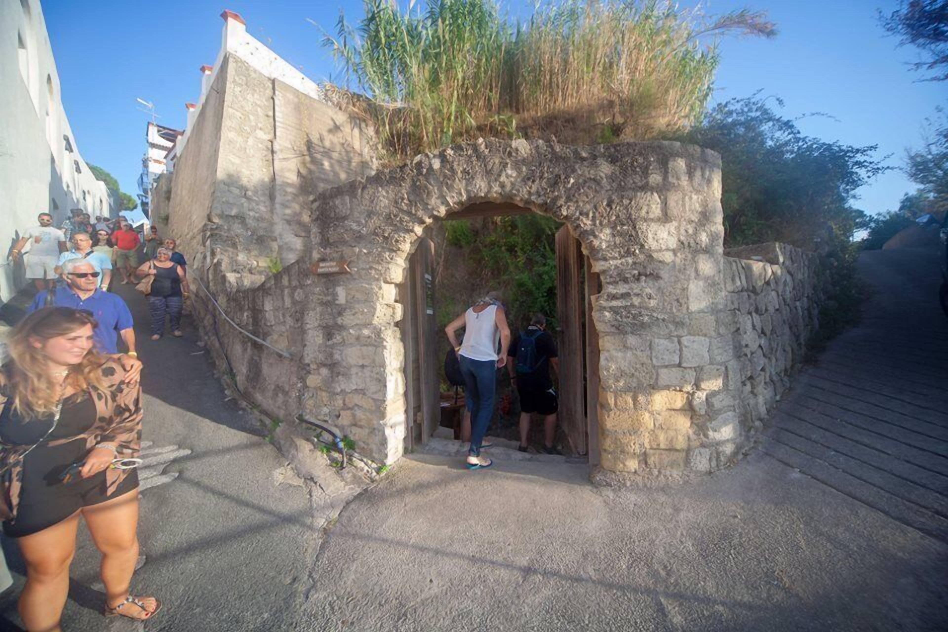 Ein steinerner Bogen führt in eine enge Gasse, durch die Touristen gehen.