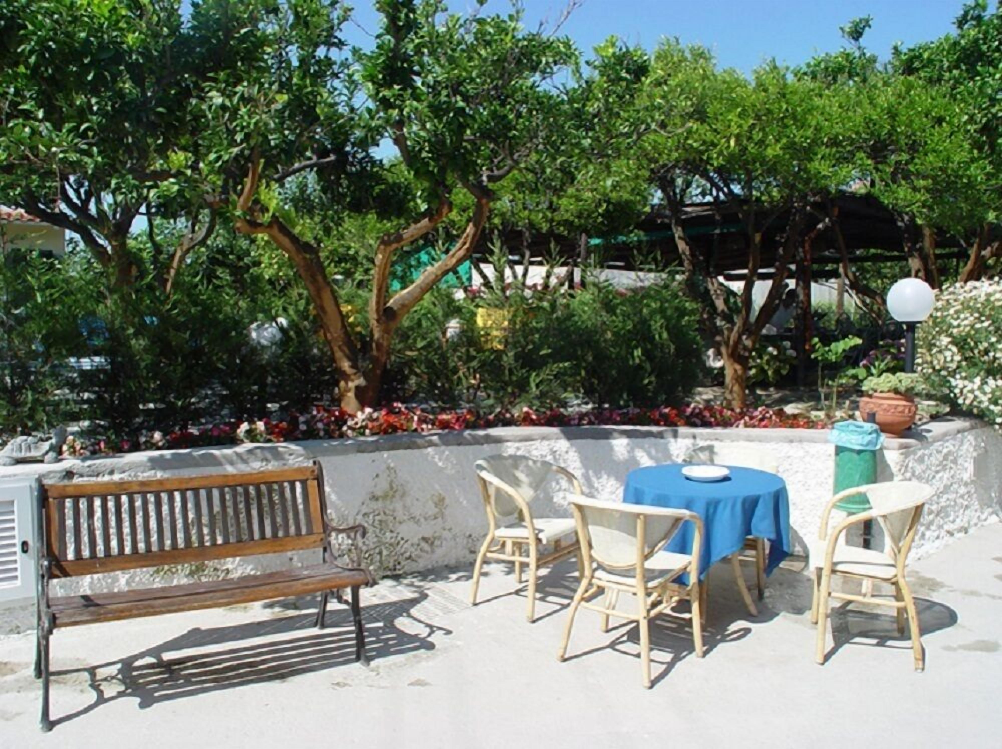 An outdoor seating area with a bench and tables, surrounded by trees and plants.