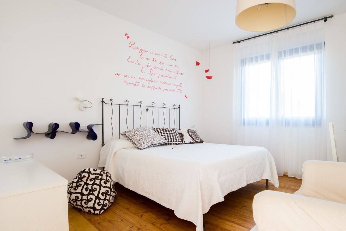 Ein Schlafzimmer mit einem Bett, einem Nachttisch, einem Sessel, einer Wandheizung und einem Fenster mit Vorhängen.