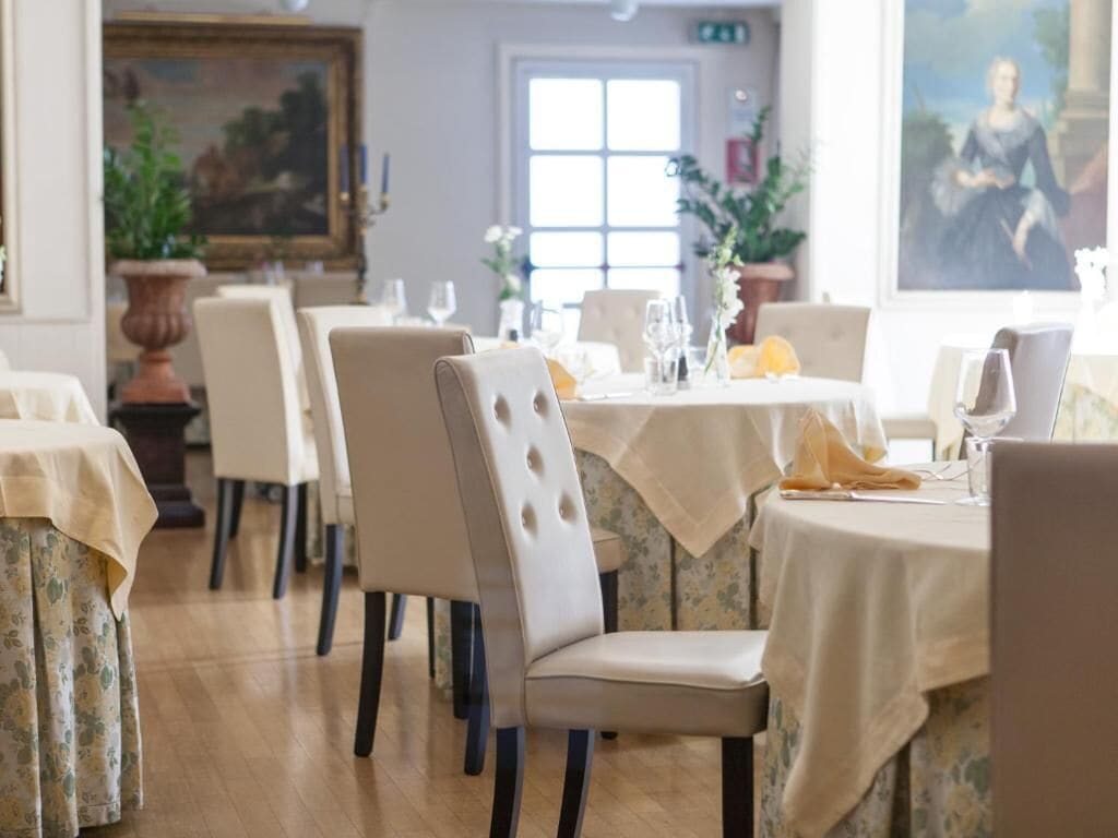A dining area with tables set for two, featuring cream-colored tablecloths and matching chairs.