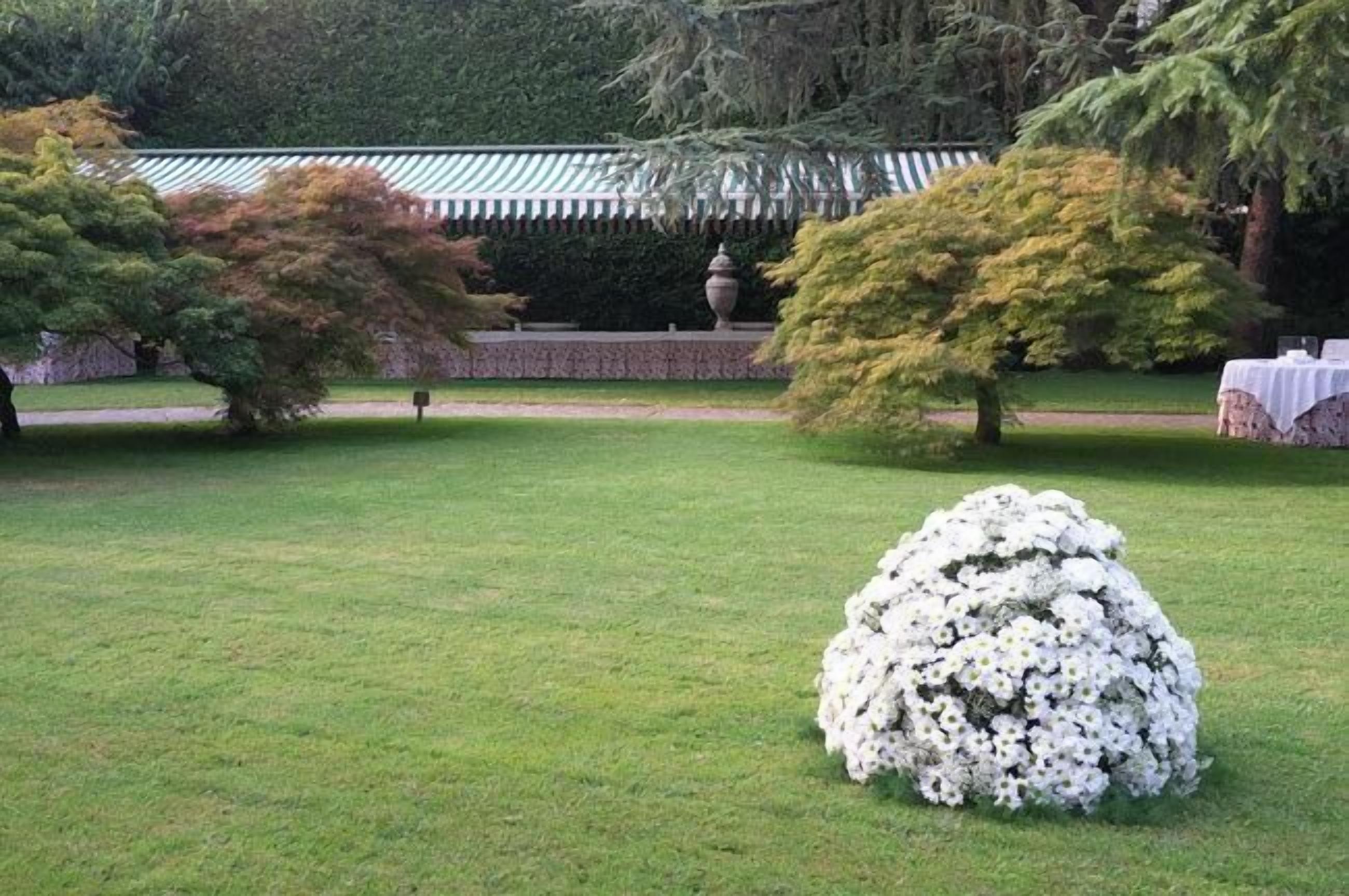 A well-maintained garden with a large white flower arrangement in the foreground, a stone wall, and a traditional building with a green roof in the background.