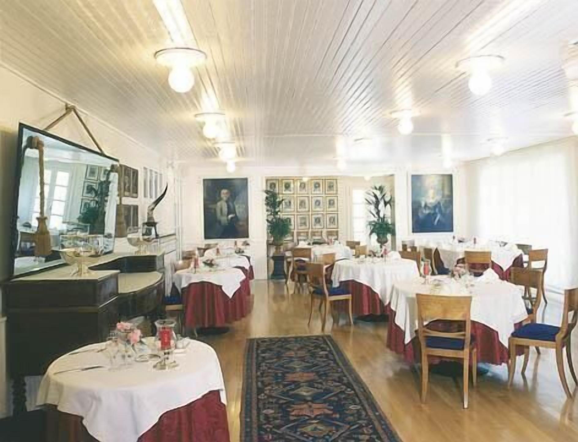 Un comedor con varias mesas dispuestas para el servicio, un espejo grande y obras de arte enmarcadas en las paredes.