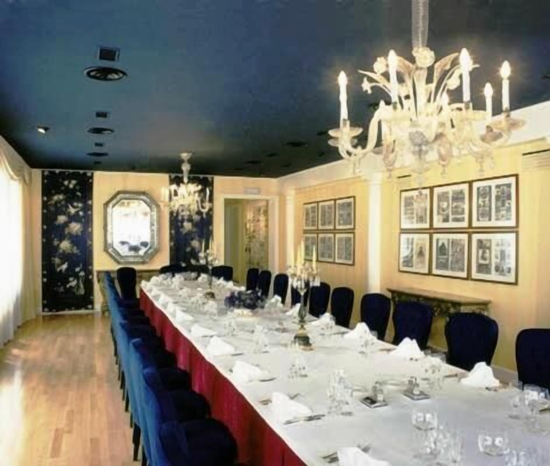 A long dining table set for a formal event, with chairs on both sides and a chandelier above.