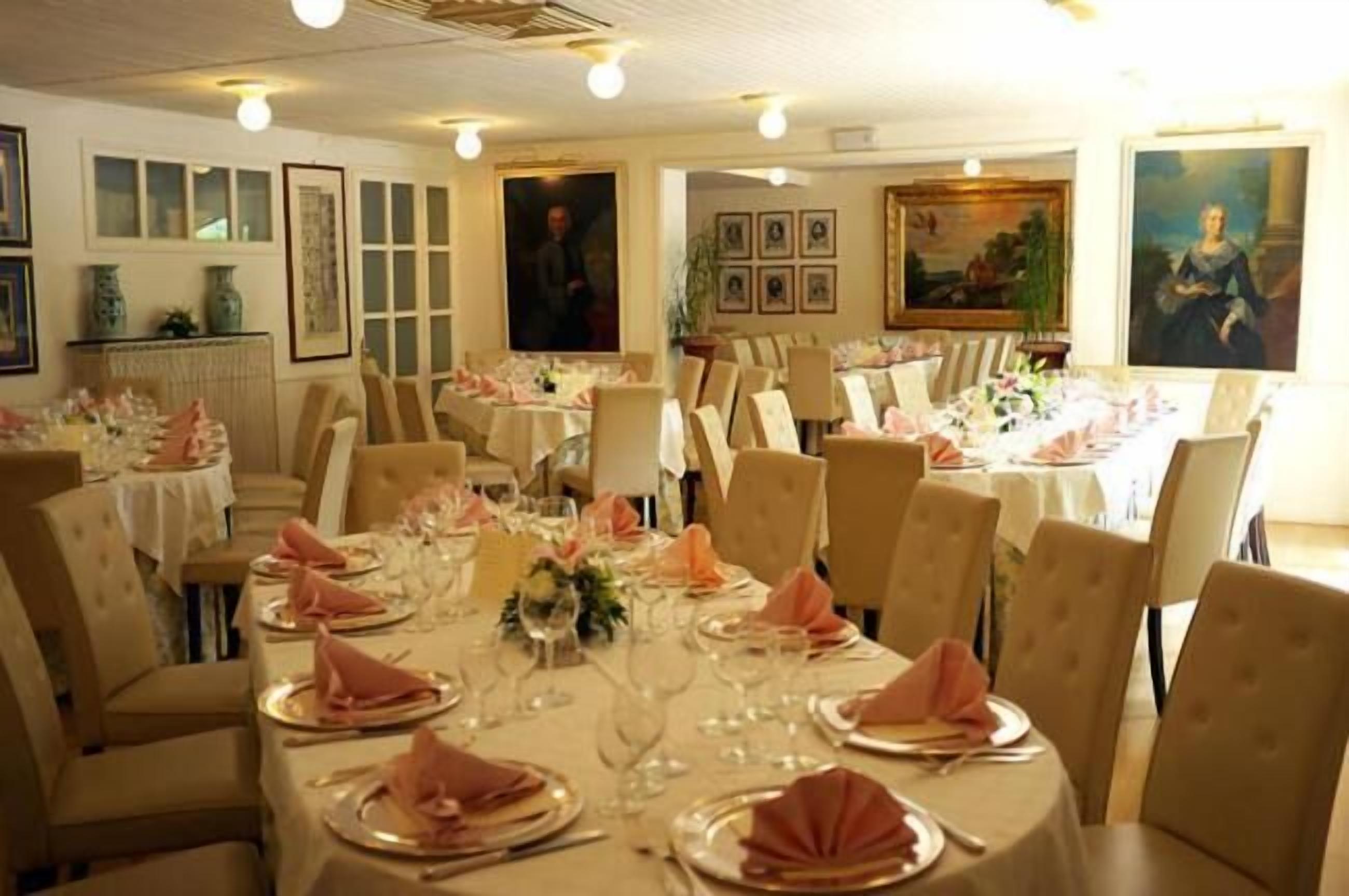 Uma sala de jantar com várias mesas preparadas para uma refeição formal, apresentando cadeiras e mesas organizadas com toalhas e guardanapos dobrados.
