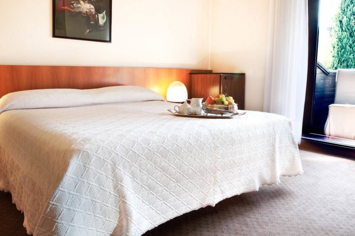 A neatly made bed with a white quilt, a bedside table with a lamp, and a tray with fruits and a teapot.