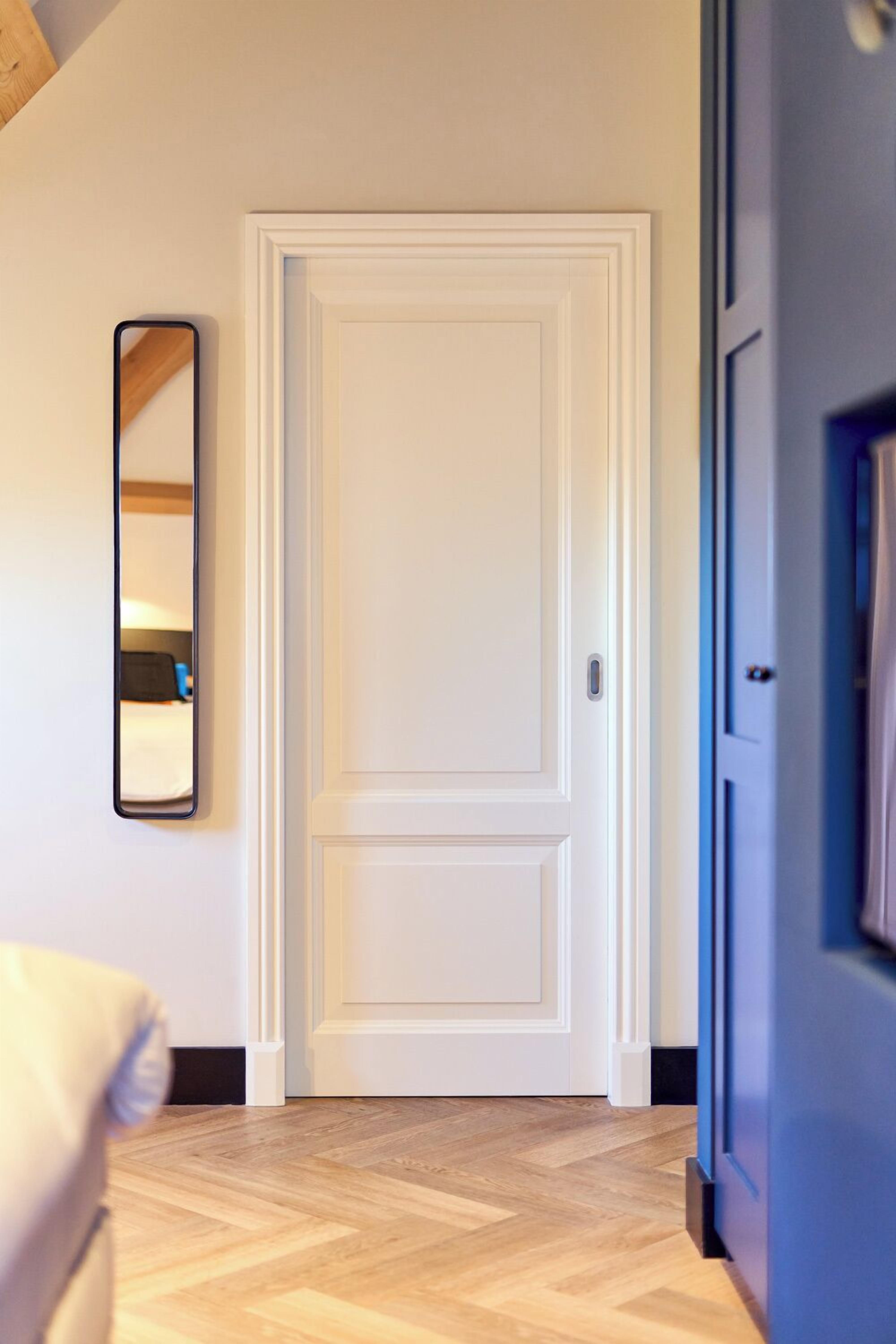 Un couloir avec une porte blanche, un miroir au mur et un plancher en bois.