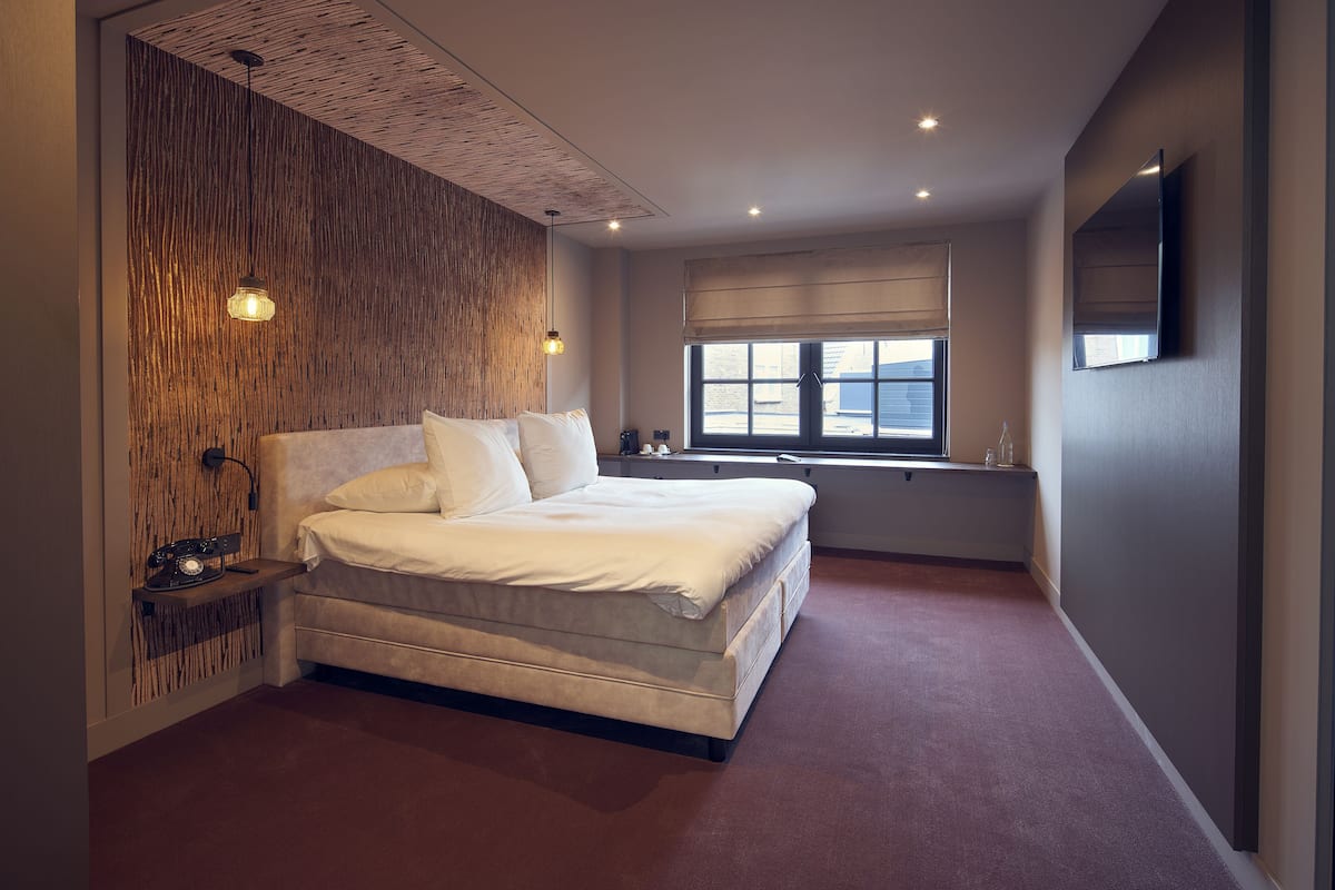 Un dormitorio moderno con una cama grande, un muro decorativo de madera, una ventana con persianas y un televisor de pantalla plana montado en la pared.