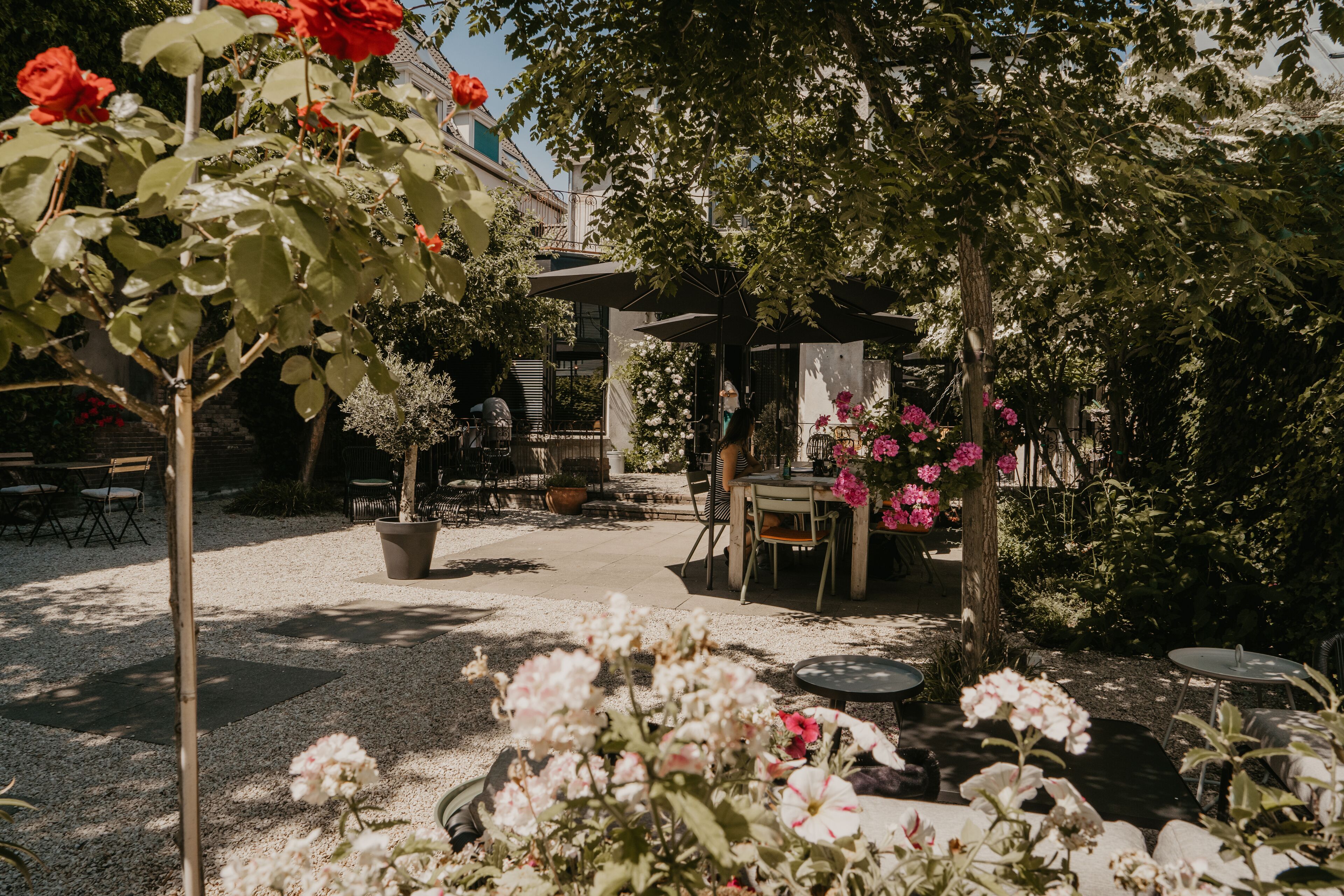 An outdoor patio area with tables and chairs, surrounded by potted plants and flowers.